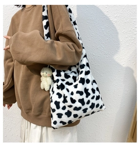 Detail of soft cow print plush tote bag with a cute bear charm on a female model
