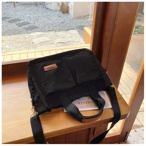 Detail of black corduroy tote bag showing large front pockets and brown leather brand label