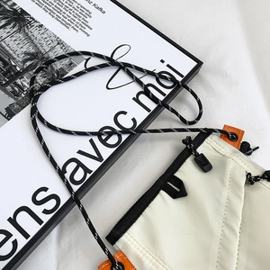 Close-up of cream nylon crossbody bag with woven shoulder strap and orange side detail