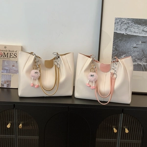Two stylish pleated tote bags with chain straps and plush charms on a vintage cabinet