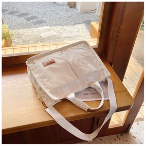 Detail of cream corduroy tote bag showing side pockets and brown leather fashion tag