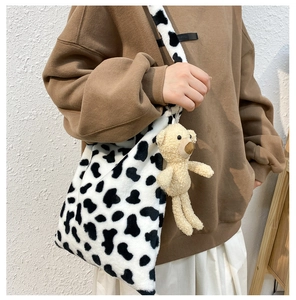 Detail view of cow print plush crossbody bag with cute teddy bear charm accessory