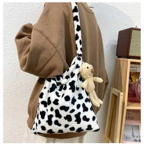 Detail of plush cow print shoulder bag with a cute brown teddy bear keychain accessory