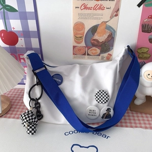 Close-up of white nylon messenger bag with blue strap and plush bear keychain accessory