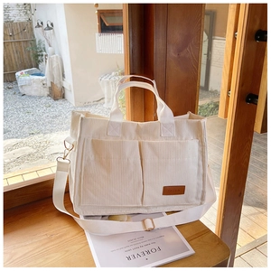 Detail of corduroy tote bag featuring front pockets, leather patch and adjustable strap