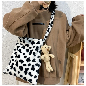 Detail of soft faux fur cow print crossbody bag with cute teddy bear plush charm accessory