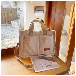 Detail of beige corduroy tote bag showing front pockets and adjustable strap on a window