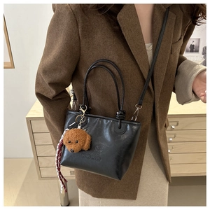 Close-up of black leather bucket bag with letter embossing and cute dog plush charm