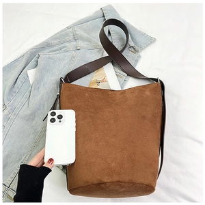 Size reference of brown matte bucket bag with wide shoulder strap beside a smartphone