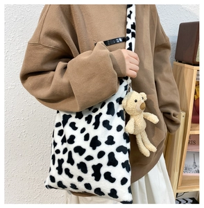 Detail of cow print plush tote bag featuring a cute beige bear charm and soft fur texture