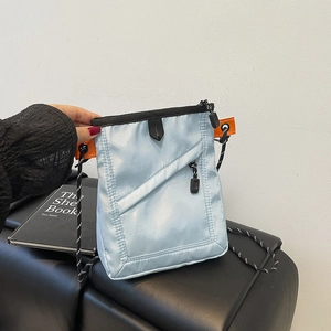 Detail of light blue nylon crossbody bag with zipper pocket and orange woven strap accents