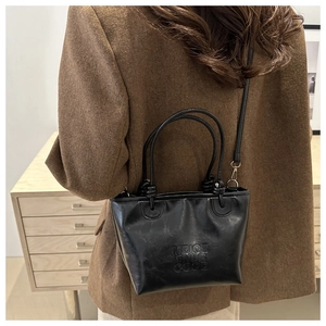 Detail of black glossy leather handbag with embossed letters and metal buckle closure