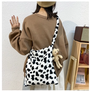 Detailed back view of a plush cow print crossbody bag with a cute bear charm accessory
