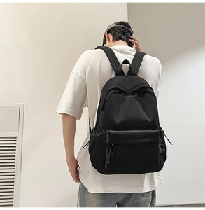 Detail view of a minimalist black canvas backpack showing the side pocket with adjustable drawstring