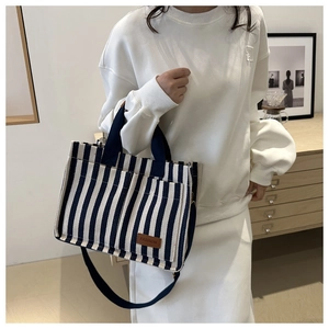 Detail of blue striped canvas tote bag with front pockets and fashion leather label