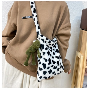 Detail of plush cow print crossbody bag with cute green frog pendant and soft fuzzy strap