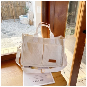Detail view of beige corduroy tote bag featuring dual front pockets and brown fashion leather tag