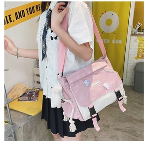Pink and white canvas messenger bag with a plush bear charm and cartoon pins detail