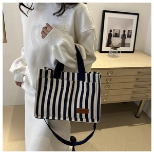 Detailed close-up of a blue striped canvas tote bag with a brown leather FASHION patch