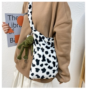Close-up of fluffy cow print crossbody bag featuring a cute green frog plush pendant