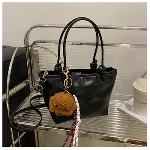Detail of black leather handbag with embossed letters and cute brown teddy bear charm