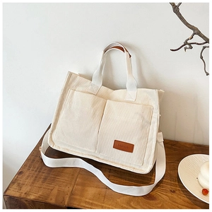 Detail of cream corduroy tote bag featuring dual front pockets and adjustable strap