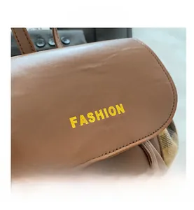 Detail of brown leather backpack with yellow Fashion lettering and plaid fabric sides