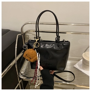 Detail of black PU leather tote bag with embossed letters and brown plush dog charm