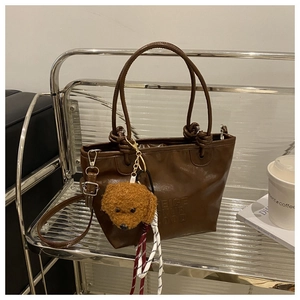 Detail of dark brown leather tote bag with embossed letters and plush dog pendant
