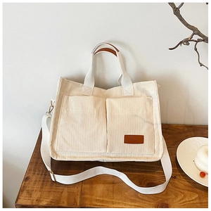 Detail of corduroy tote bag featuring front pockets and fashion leather label on wood