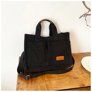 Detail of black corduroy tote bag showing symmetry pockets and orange leather fashion label
