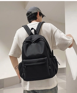 Rear view of a black canvas backpack worn by a model in a minimalist setting