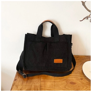 Detail of black corduroy tote bag showing front pockets and leather fashion label