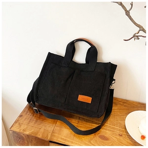 Detail view of black corduroy tote bag with dual handles and orange fashion logo