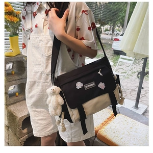 Detail of canvas messenger bag with cartoon badges and a white plush bear pendant