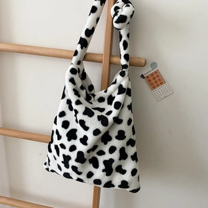 Plush cow print shoulder bag with knotted strap hanging on a wooden ladder background