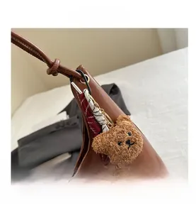 Close-up of brown leather tote bag featuring a knotted strap and a cute plush bear charm