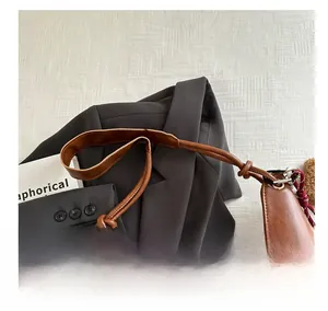 Detail of a brown crescent shoulder bag featuring a unique braided rope top handle design