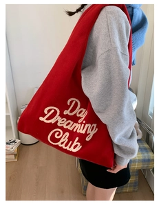 Detail of red plush tote bag featuring white cursive Day Dreaming Club embroidery text