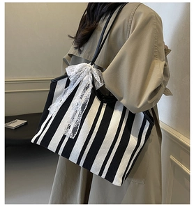 Detail view of striped canvas tote bag with white lace bow on shoulder of a model