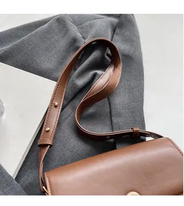 Detail of a brown leather shoulder bag with adjustable strap and gold rivet accents
