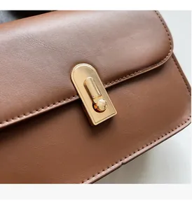 Detail of a brown leather square bag featuring a sleek gold rectangular metal clasp and stitching