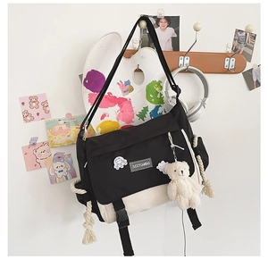Detail of canvas messenger bag with bear charm and badge on white wall background
