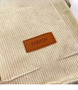 Detail of beige corduroy shoulder bag showing brown leather FASHION label and stitching