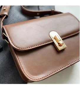 Close-up of caramel brown leather square bag showing lychee texture and gold buckle detail
