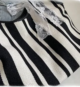 Close-up of black and white striped canvas tote bag with elegant white lace bow detail