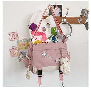 Detail of pink canvas messenger bag with plastic buckle, plush bear, and cute badges