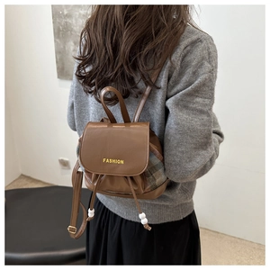 Detail view of mini backpack with brown leather flap and colorful plaid pattern fabric