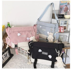 Detailed view of canvas messenger bags in pink, blue, and black with bear charms