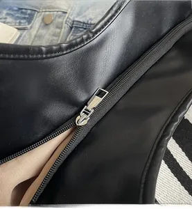 Close-up of smooth silver metal zipper on a black synthetic leather tote bag with beige lining